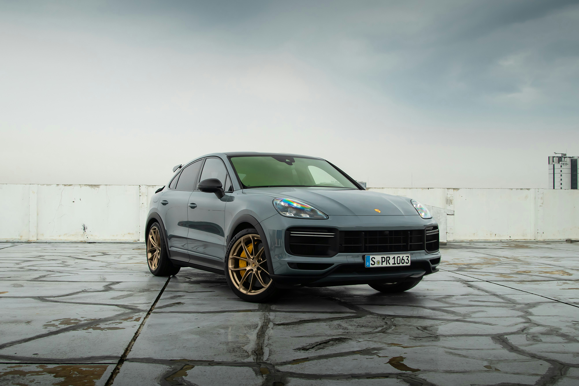 A light grey Porsche cayenne turbo gt being shown while being on top of a building and the background being the sky